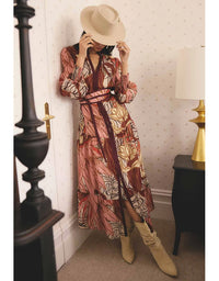 Person wearing a patterned dress and beige hat in a room with wallpapered walls.