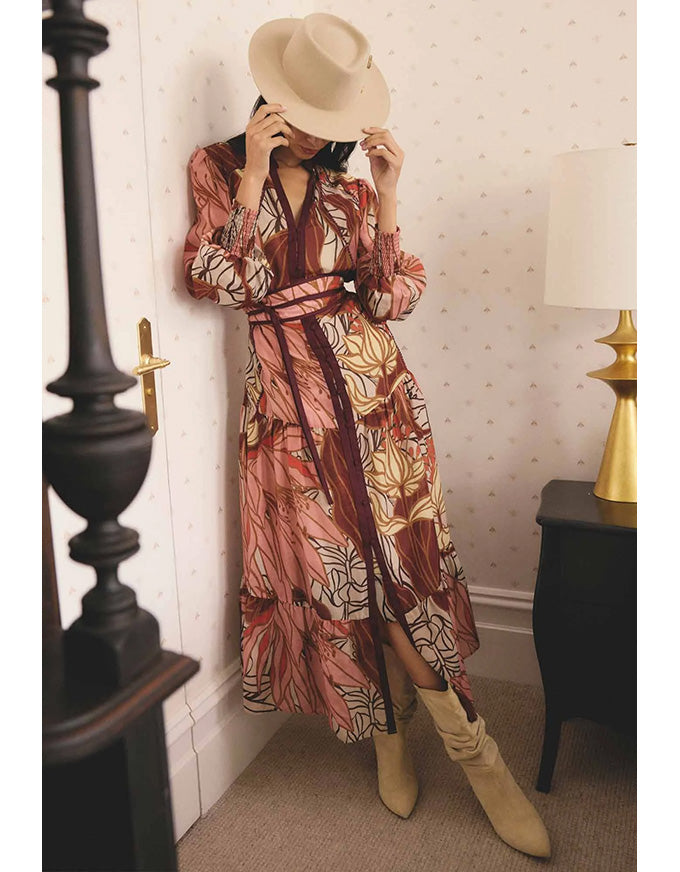 Person wearing a patterned dress and beige hat in a room with wallpapered walls.