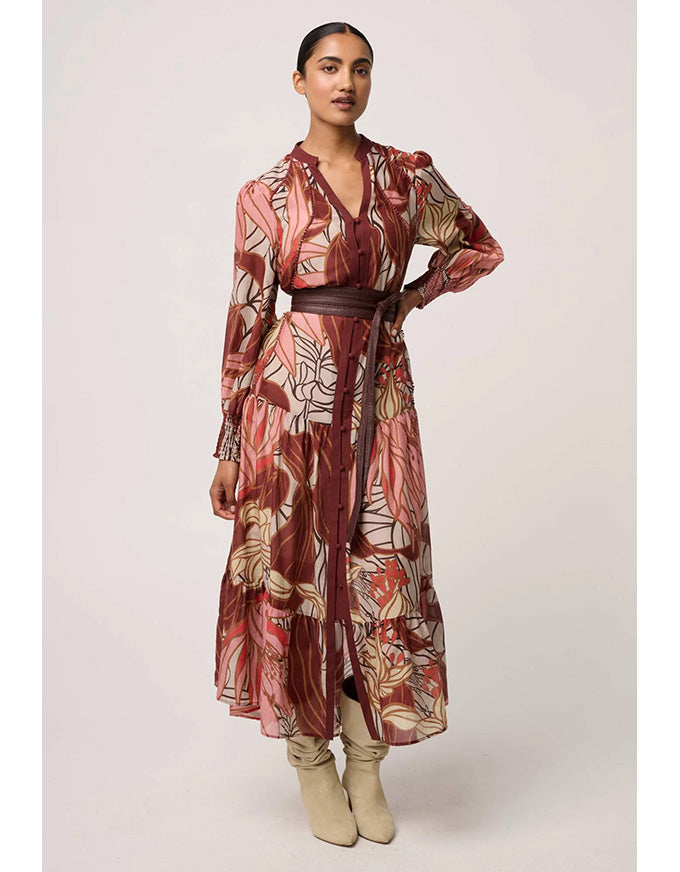 Woman wearing a long, patterned dress with a belt on a plain background