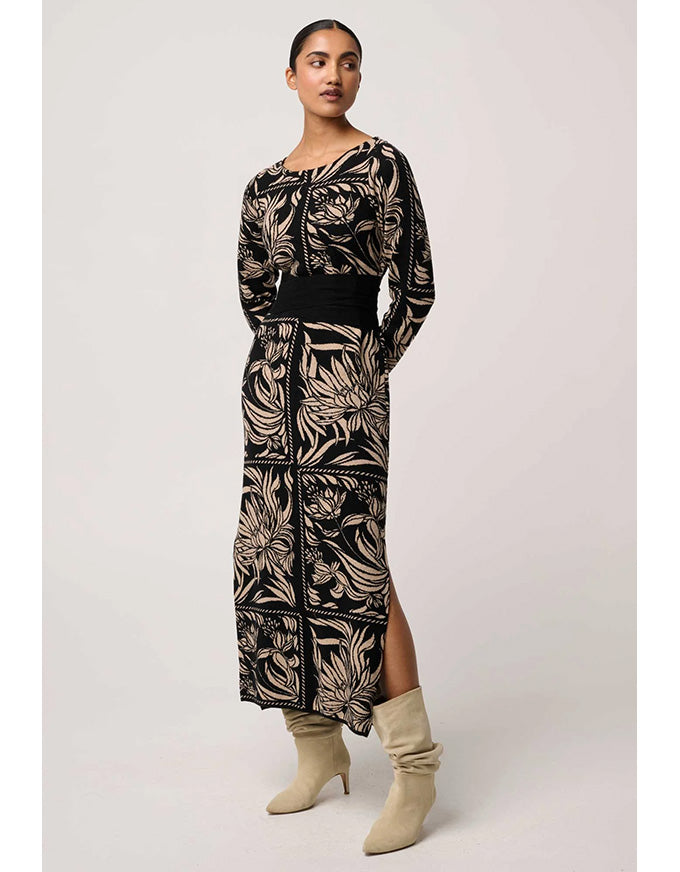 Woman wearing a long, patterned dress with beige boots on a white background