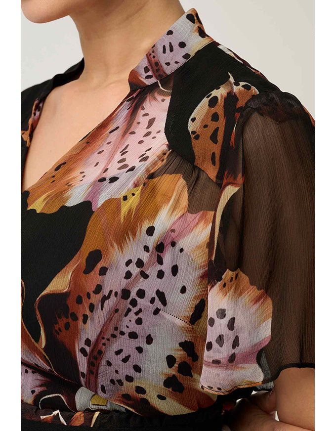 A close-up of a woman wearing a sheer black dress with a large abstract floral print in orange, brown, pink, and black.