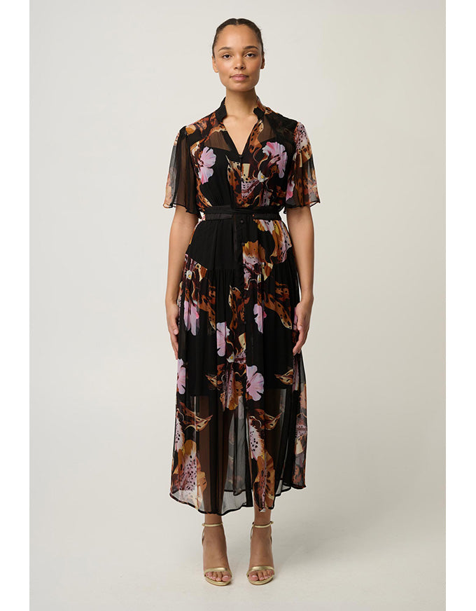 A woman modeling a black midi dress with a pink and brown floral print, sheer short sleeves, and a matching black belt, set against a plain light gray studio background.