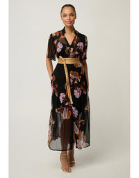 A woman models a black midi wrap dress with a vibrant floral print in pink, purple, and orange, featuring short flutter sleeves, a V-neckline, and a tan tie belt at the waist.
