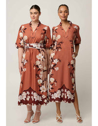 Two models wearing matching rust-orange floral midi dresses with white and cream flowers, dark brown leaves, and a patterned waist belt, posed against a light gray studio background.
