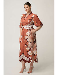 A woman modeling a rust-orange midi wrap dress with a white, black, and burgundy floral print, featuring a tie waist belt and short puff sleeves, set against a plain light gray studio background.