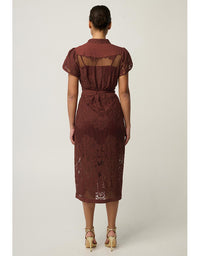 A woman viewed from the back wearing a rust-brown lace midi dress with short puff sleeves, sheer mesh back panels, and a matching fabric tie belt, paired with beige high-heeled sandals against a light gray studio background.