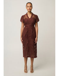 A woman modeling a short-sleeve midi dress in a deep burgundy lace and mesh fabric, standing against a neutral light gray studio background.