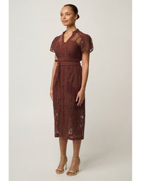 A woman modeling a rust-brown lace midi dress with short puff sleeves, a V-neckline, and a matching fabric tie belt, paired with gold high-heeled sandals against a light gray studio background.