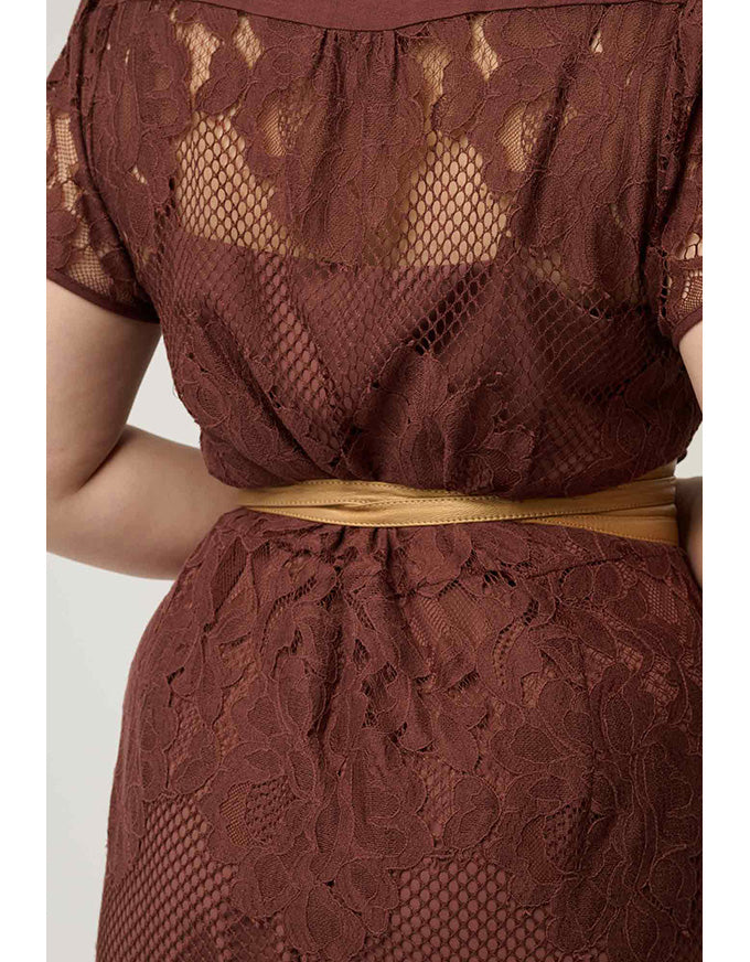 Close-up of a woman wearing a brown lace dress with a sheer mesh back panel and a thin tan waist sash.