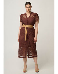 A woman modeling a brown lace midi dress with sheer puff sleeves, a button front, and a tan tie belt, photographed against a plain light gray studio background.