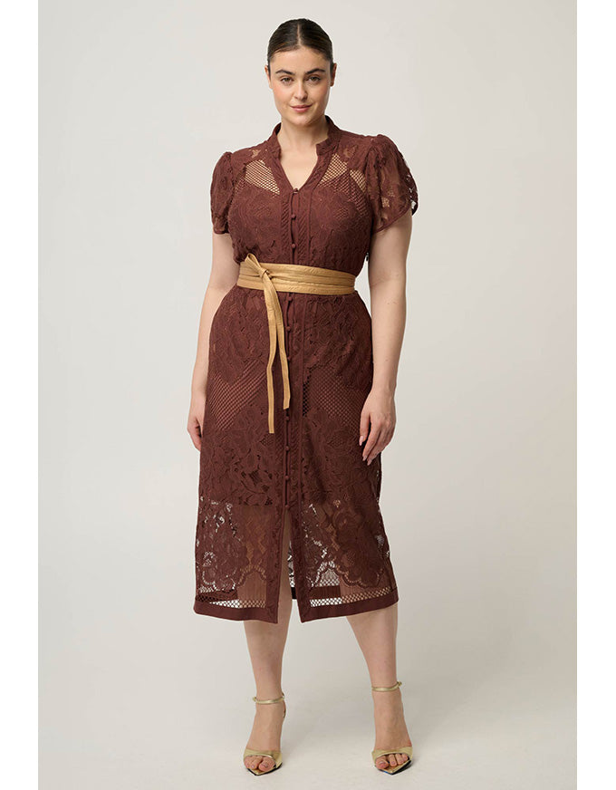 A woman modeling a brown lace midi dress with sheer puff sleeves, a button front, and a tan tie belt, photographed against a plain light gray studio background.
