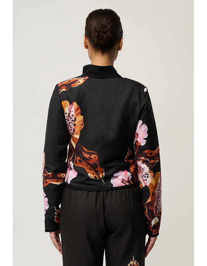 A model shown from the back wearing a black mock-neck long-sleeve top with a bold orange, pink, and brown floral print on the shoulders and sleeves, paired with black pants.