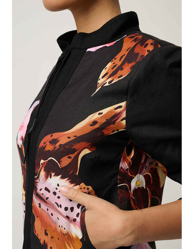 A close-up of a model wearing a black short-sleeve top with a bold orange, brown, and pink abstract floral print on the front and sleeves.
