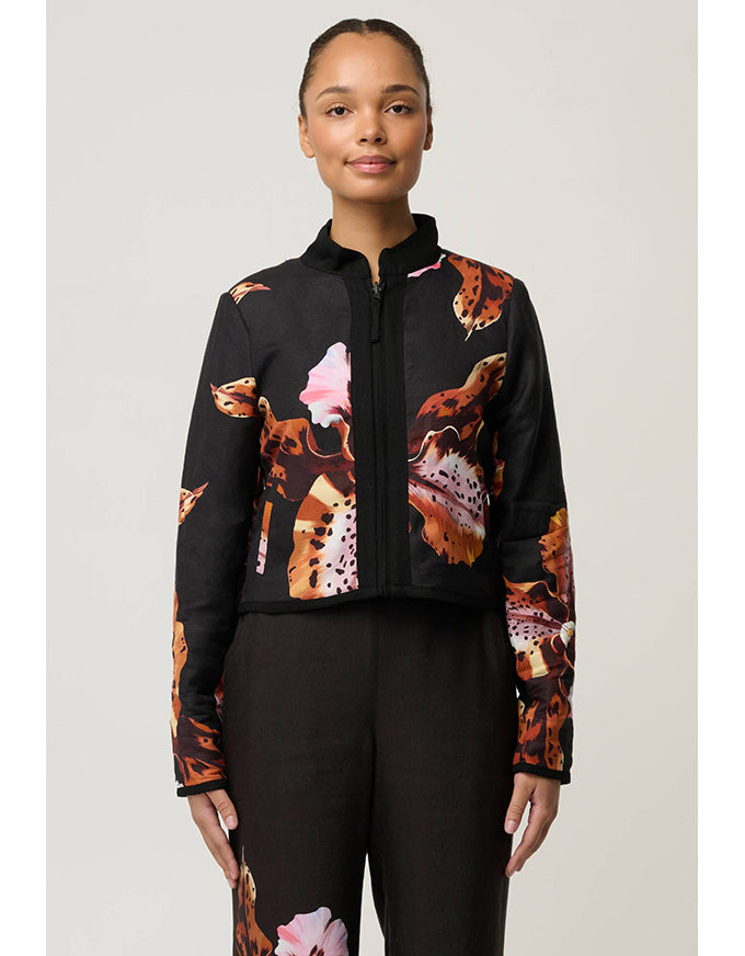 A model wearing a black cropped zip-up jacket with a vibrant orange, brown, and pink abstract floral print, paired with black pants, against a light gray studio background.