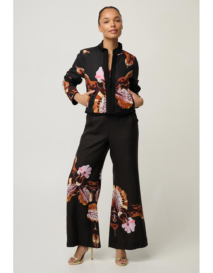 A model stands against a light gray studio background wearing a matching black two-piece set with a butterfly print. The set includes a cropped button-front jacket and wide-leg trousers, featuring orange, brown, and pink butterfly motifs.
