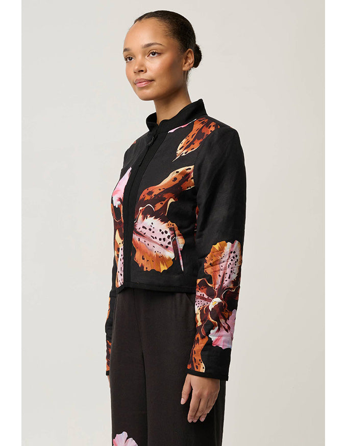 A model wearing a black cropped jacket with a vibrant orange, pink, and brown abstract floral print, paired with black trousers, against a light gray studio background.