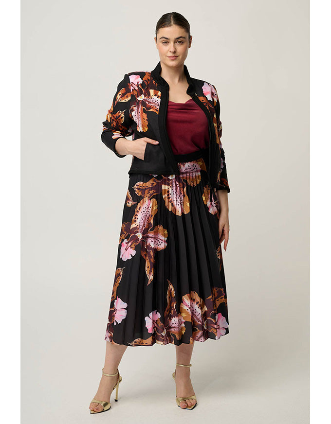 A woman models a black midi skirt with a pink and brown floral print, styled with a matching black blazer over a burgundy top, on a light gray studio background.