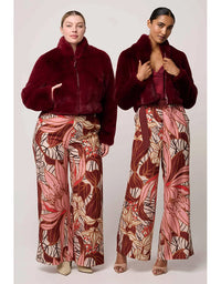 Two models wearing matching outfits with a burgundy fur coat and patterned pants on a white background.