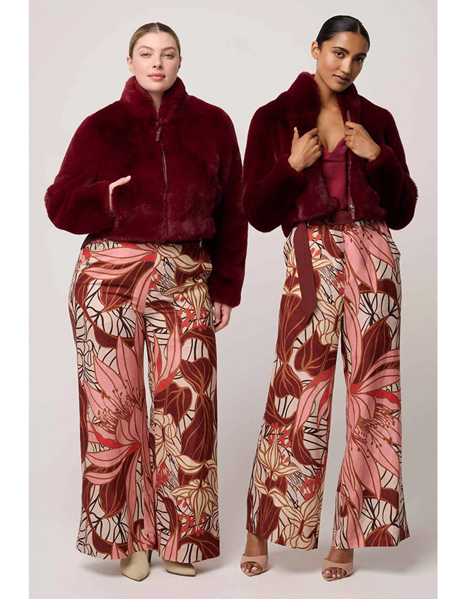 Two models wearing matching outfits with a burgundy fur coat and patterned pants on a white background.