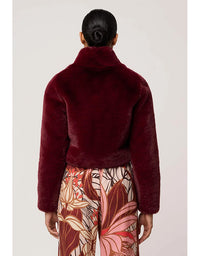 Person wearing a burgundy fuzzy jacket with floral pants on a plain background