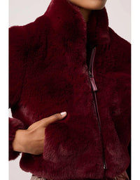 Close-up of a burgundy faux fur jacket with a hand touching the fabric.