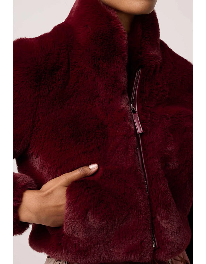 Close-up of a burgundy faux fur jacket with a hand touching the fabric.