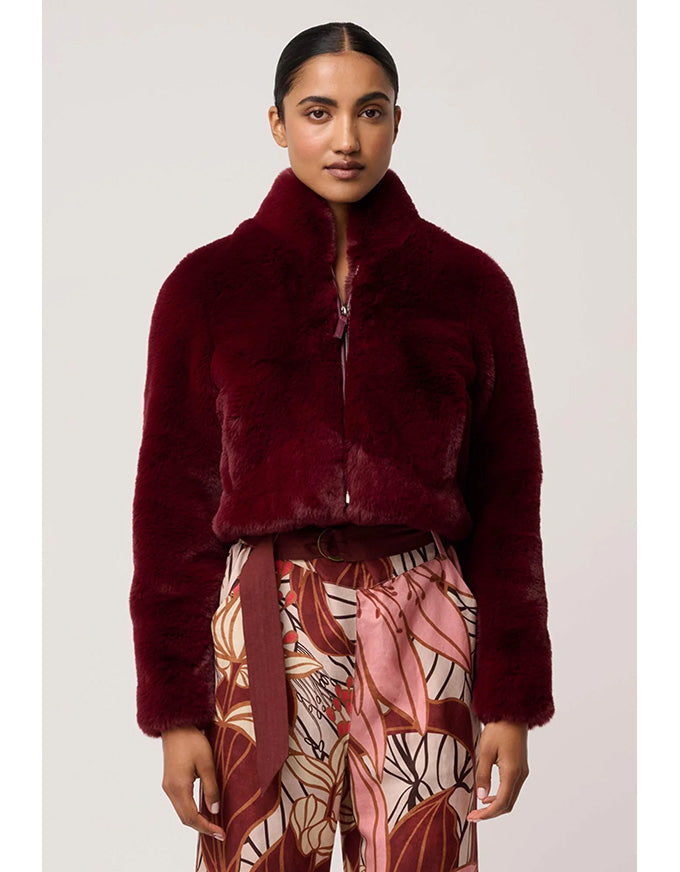 Woman wearing a burgundy faux fur jacket with a patterned skirt on a plain background