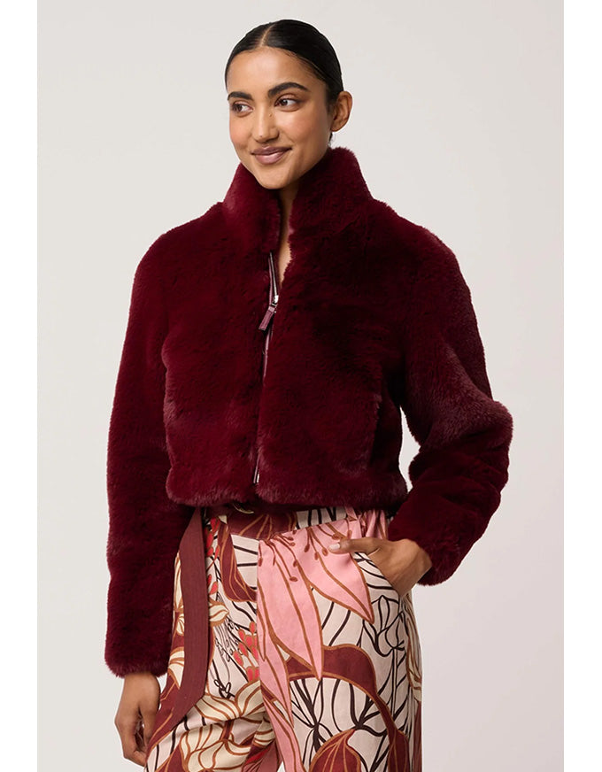 Woman wearing a burgundy faux fur jacket with a neutral background