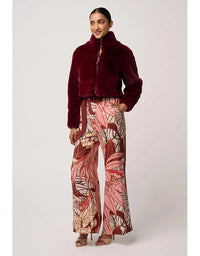 Woman wearing a burgundy fur coat and patterned pants on a white background