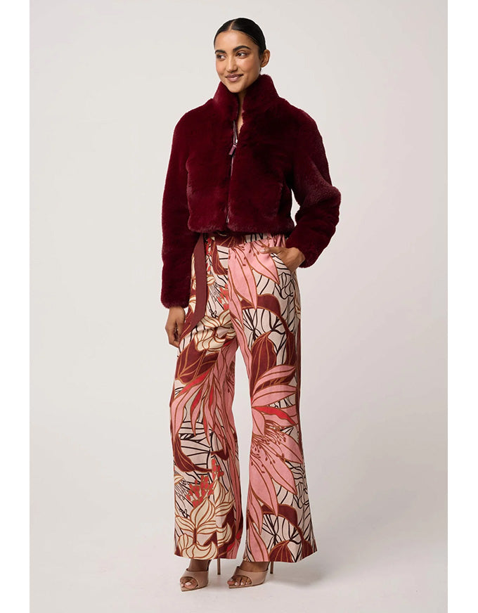 Woman wearing a burgundy fur coat and patterned pants on a white background
