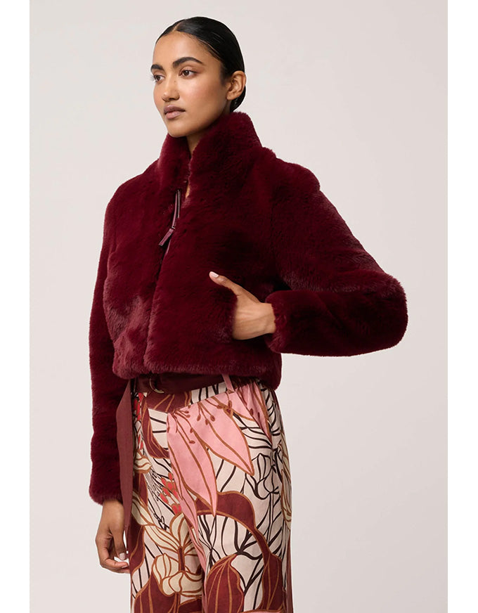 Woman wearing a burgundy faux fur jacket with a patterned skirt on a light background