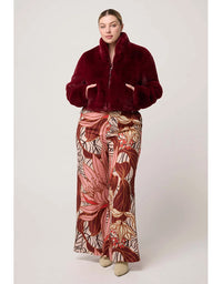 Woman wearing a burgundy fur coat and a long, patterned skirt on a white background