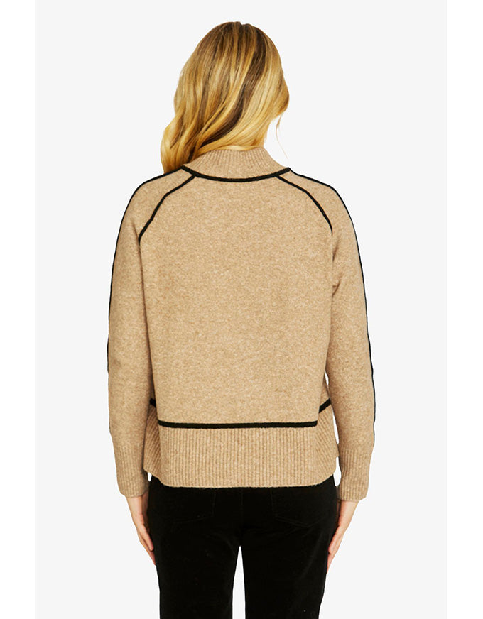 Beige sweater with black accents worn by a person on a white background