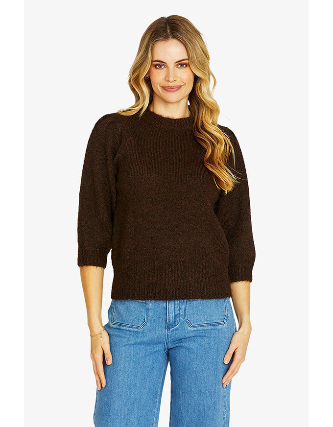 Woman wearing a brown sweater and blue jeans on a white background