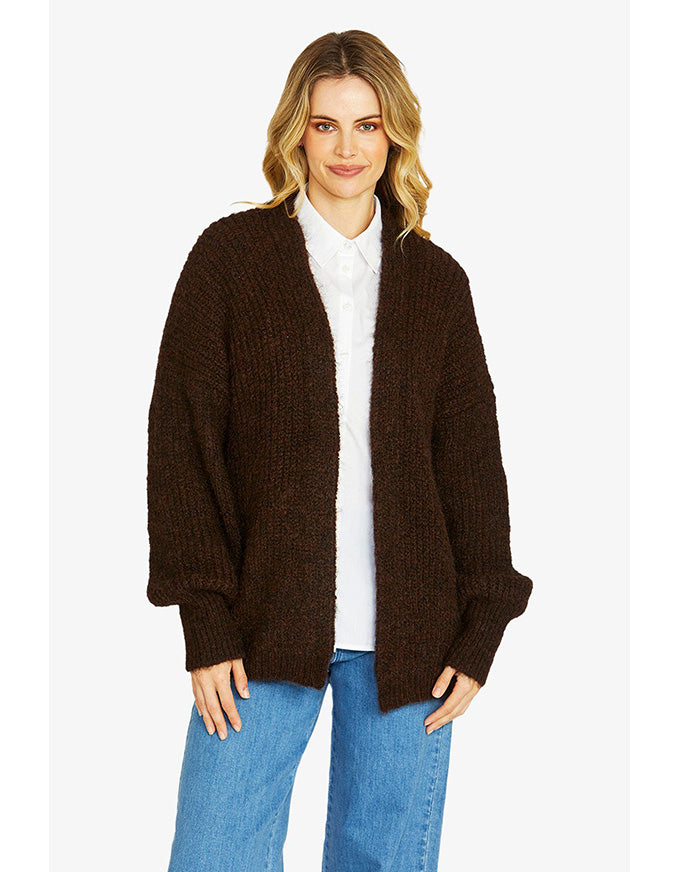 Woman wearing a brown cardigan over a white shirt and blue jeans on a white background