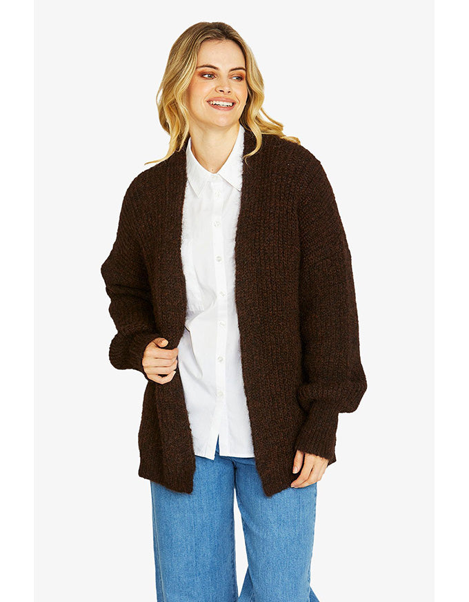 Woman wearing a brown cardigan over a white shirt and blue jeans on a white background
