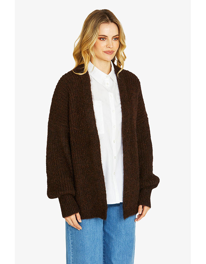 Woman wearing a brown cardigan over a white shirt and blue jeans on a white background