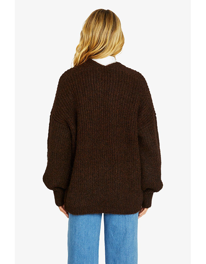 Person wearing a brown sweater and blue jeans on a white background