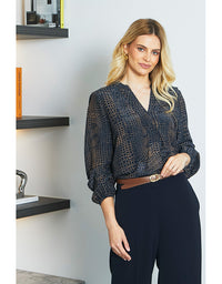 Woman wearing a dark patterned blouse and black pants in an indoor setting.
