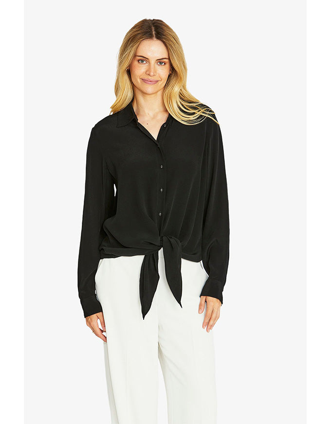 Woman wearing a black blouse with a tie waist and white pants on a white background