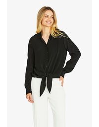 Woman wearing a black blouse with a tie waist and white pants on a white background