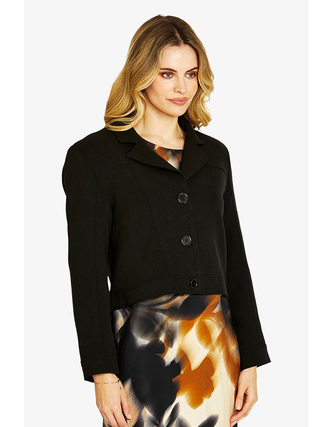 Woman wearing a black jacket over a tie-dye skirt on a white background
