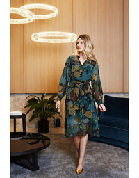 Woman in a floral dress standing in a modern interior setting with wooden walls and a blue sofa.