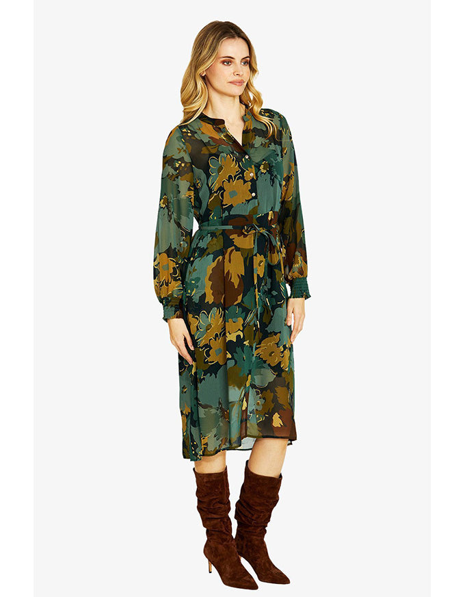 Woman wearing a green floral dress with brown boots on a white background