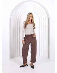 Woman wearing a beige top and brown pants standing in a white archway.