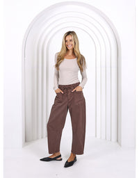 Woman wearing brown pants and a light top standing in front of a white archway.