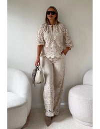 Woman in a stylish outfit with a white and beige pattern, holding a handbag in a minimalistic room.