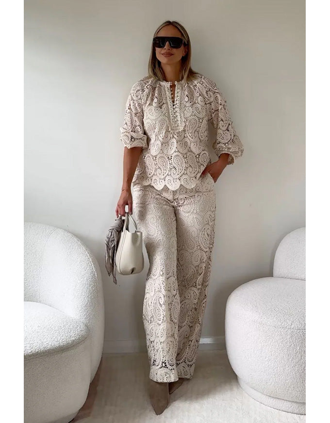 Woman in a stylish outfit with a white and beige pattern, holding a handbag in a minimalistic room.