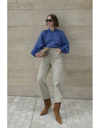 Person wearing a blue shirt, beige pants, and brown shoes against a beige wall.