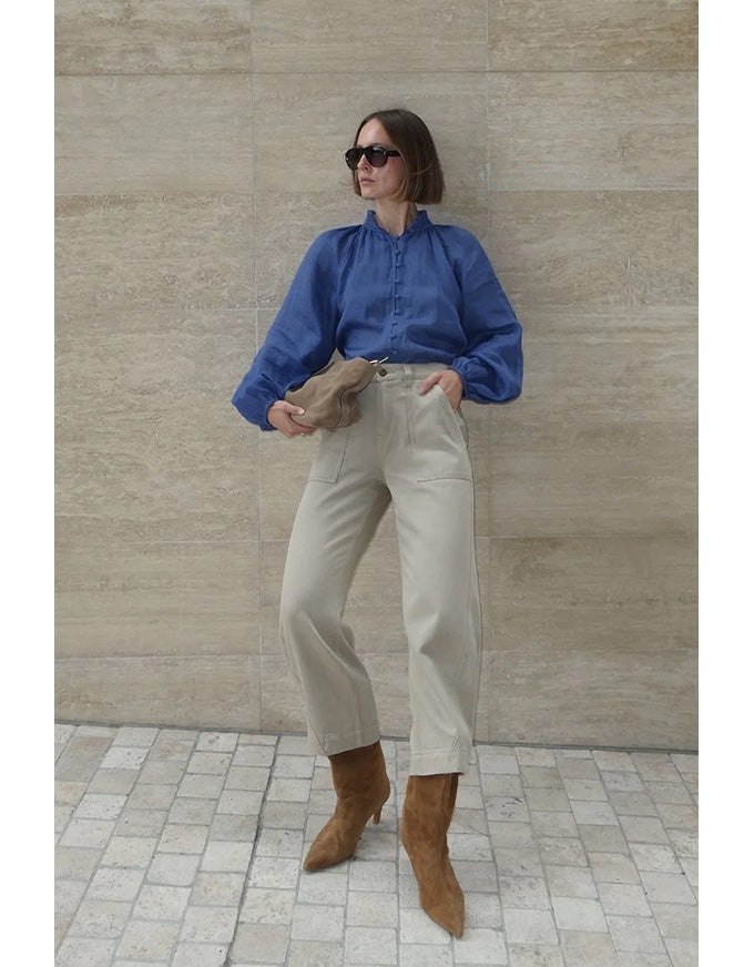 Person wearing a blue shirt, beige pants, and brown shoes against a beige wall.